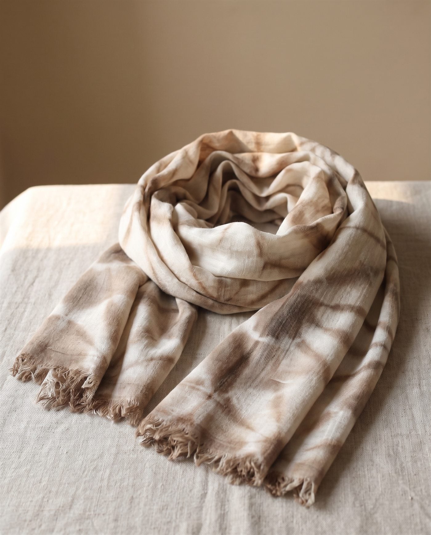 Foulard de bambula de algodón teñido con shibori en rombos marrones y blancos, doblado sobre lino natural