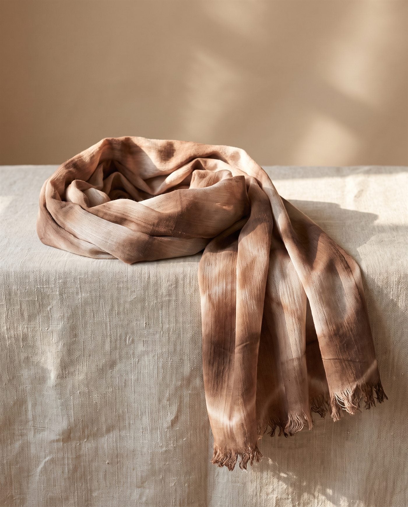 Foulard de bambula de algodón teñido con shibori en triángulos marrones y blancos, doblado sobre lino natural