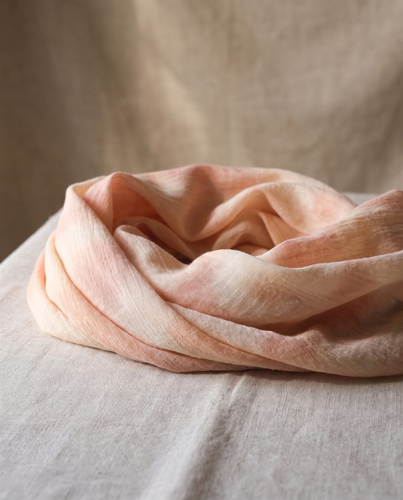 Pañoleta de bambula de algodón teñida con tinte vegetal en tonos rosados, doblada sobre lino natural
