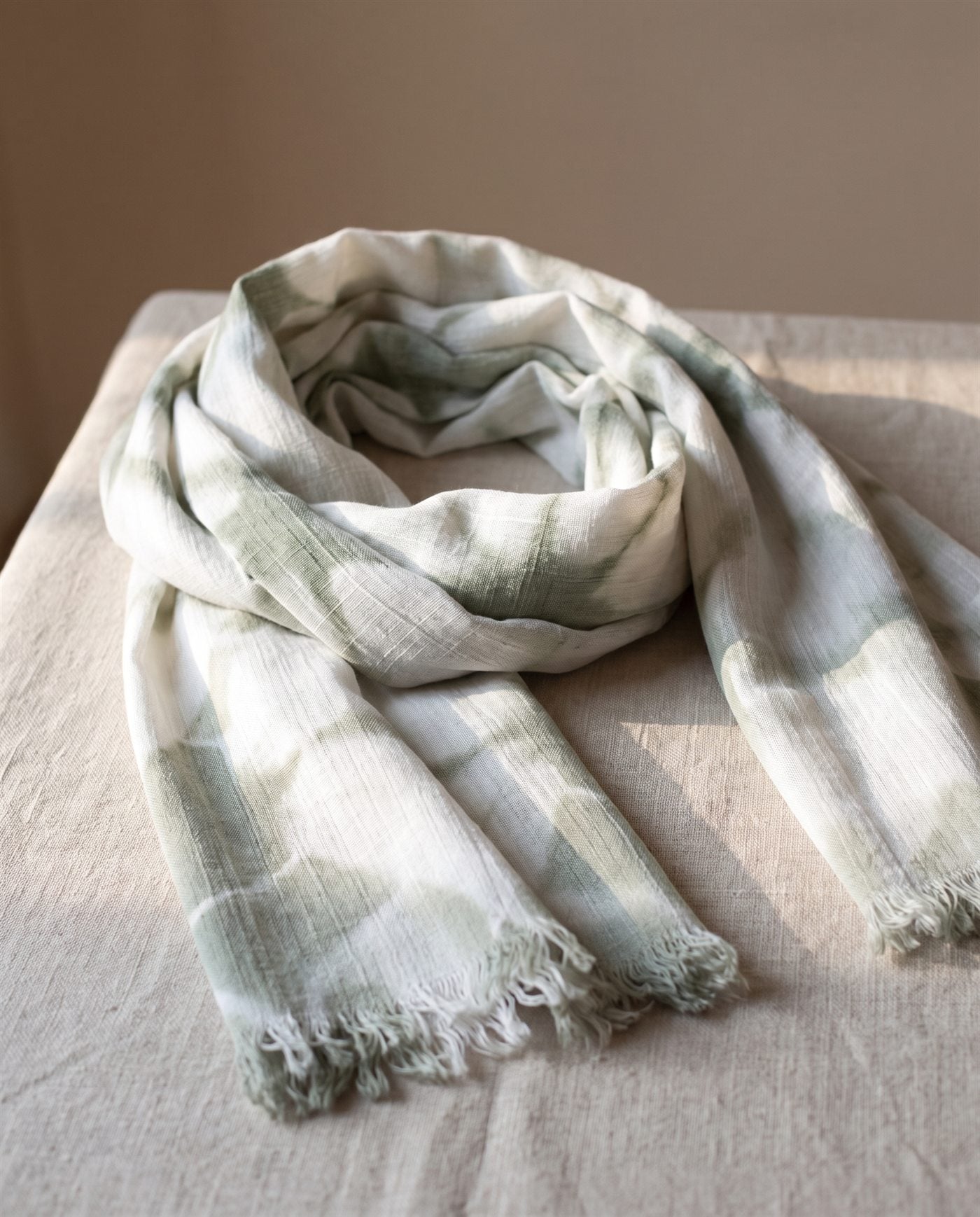 Pañuelo de bambula de algodón teñido con shibori en triángulos blancos y gris verdoso, doblado sobre lino natural