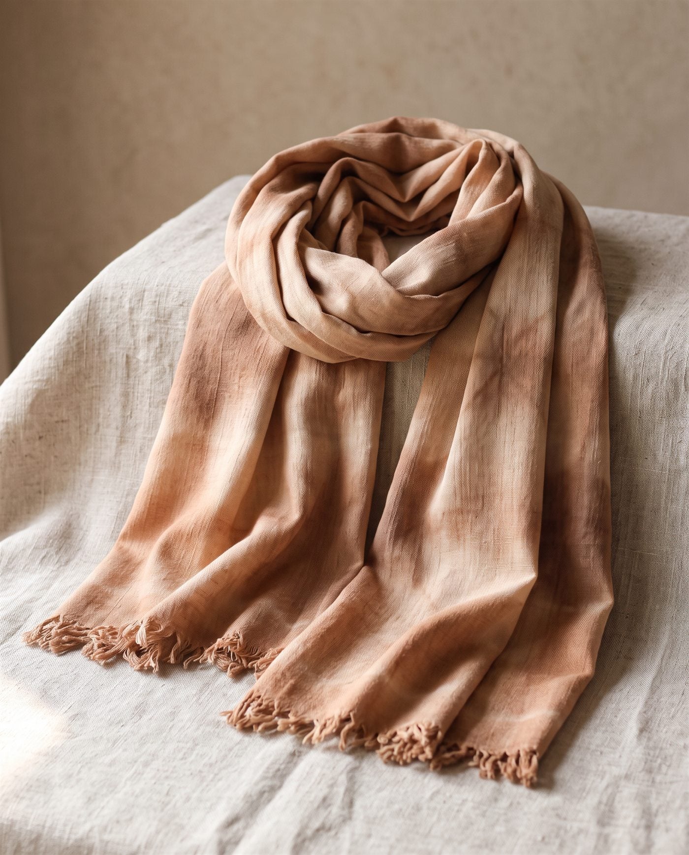 Pañuelo de bambula de algodón teñido con shibori en triángulos marrones claros, doblado sobre lino natural